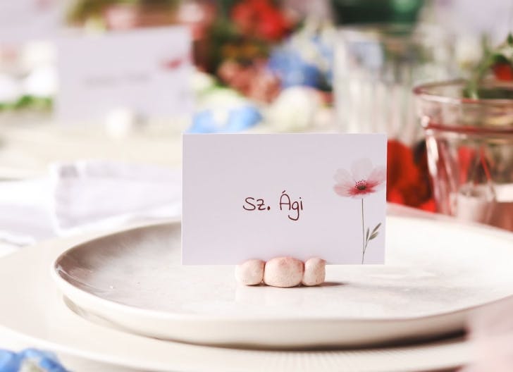 Elegant wedding placecard displayed on a wooden plate with floral napkin and vintage silverware in the background, under soft lighting.