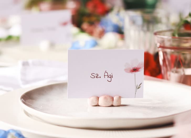 Elegant wedding placecard displayed on a wooden plate with floral napkin and vintage silverware in the background, under soft lighting.